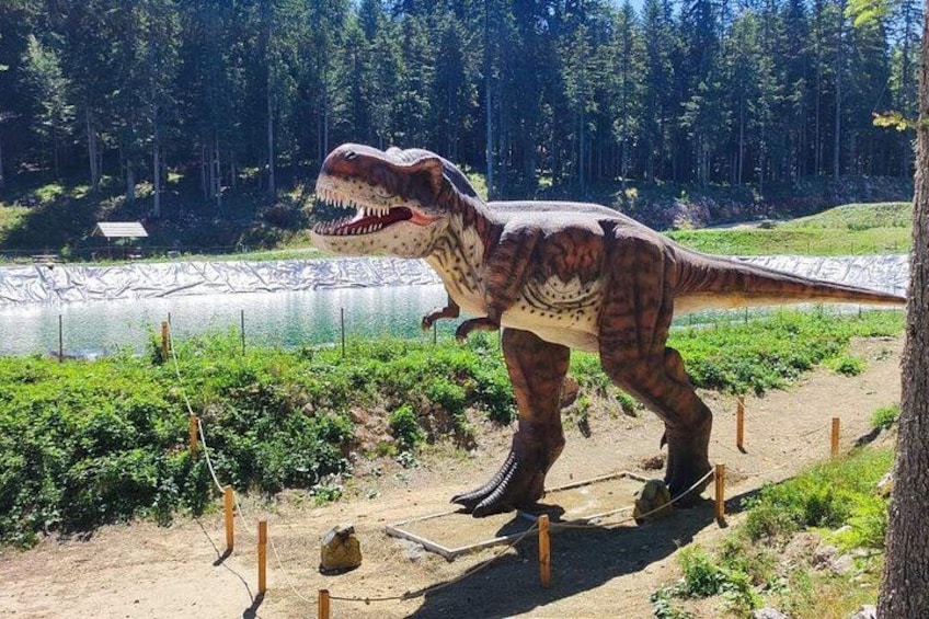 A life-sized dinosaur model near a lake with a forest in the background. 2