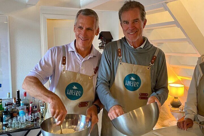 Two people wearing aprons labeled 'Lake Como Kitchen' preparing food in a kitchen. 4