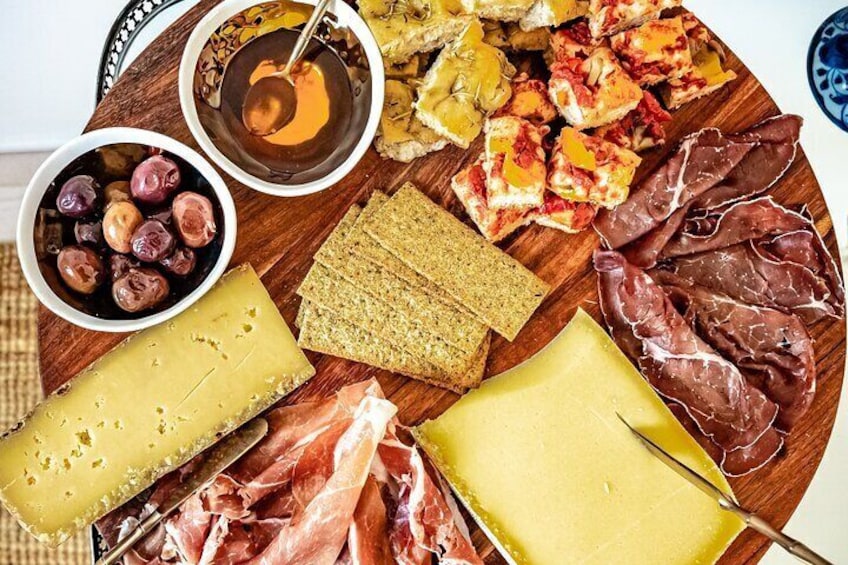 A wooden board with various cheeses, cured meats, olives, crackers, and a bowl of dip. 3