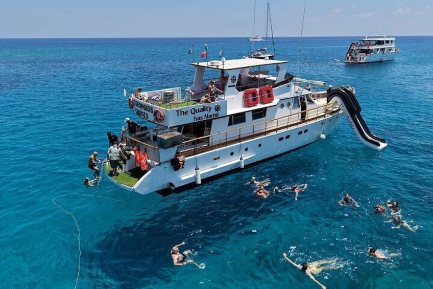 A boat with a water slide and people swimming in the ocean. 1
