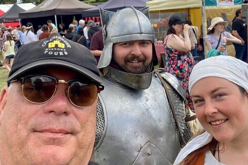 A person in medieval armor, a person in a cap, and a person in a floral dress at an outdoor event. 1