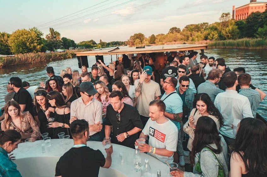A group of people gathered on a boat by a river, with a dock and trees in the background. 5