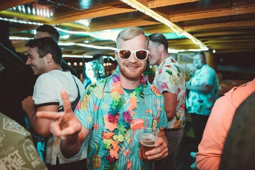 A person in a colorful floral shirt holding a drink, with other people in the background. 2