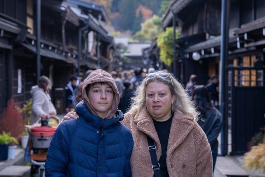 Une rue étroite bordée de bâtiments traditionnels, une personne portant une veste bleue et une autre, un manteau marron. 2