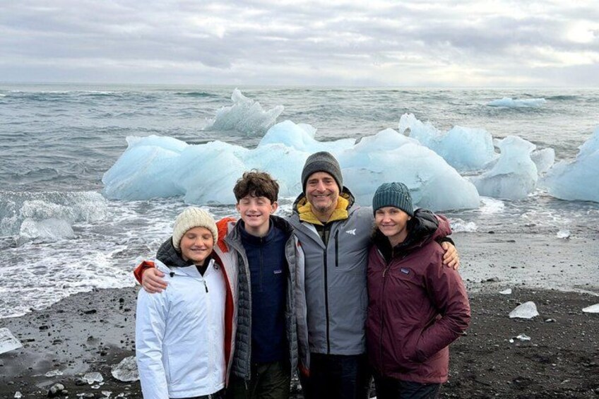 Un grupo de personas está de pie en una playa con icebergs al fondo. 2
