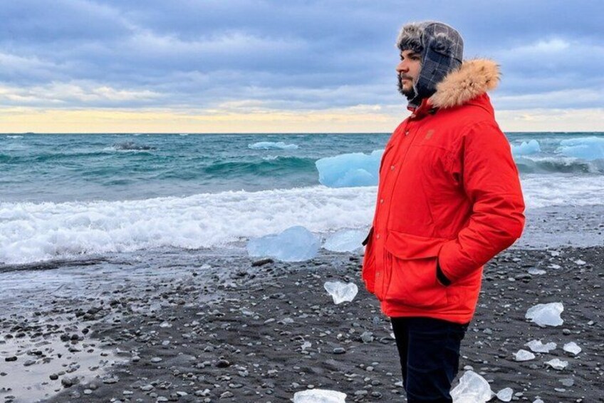 Una persona de pie en una playa rocosa con icebergs en el agua. 5