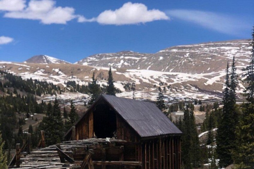 A wooden cabin with a metal roof, surrounded by snow-covered mountains and evergreen trees. 2