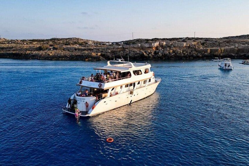 Un barco blanco con varias cubiertas y pasajeros, flotando sobre aguas azules tranquilas cerca de una costa rocosa. 5
