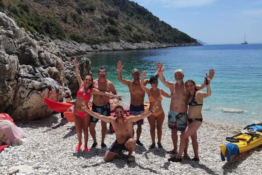 Un groupe de personnes se trouve sur une plage rocheuse, avec un bateau et un voilier en arrière-plan. 2