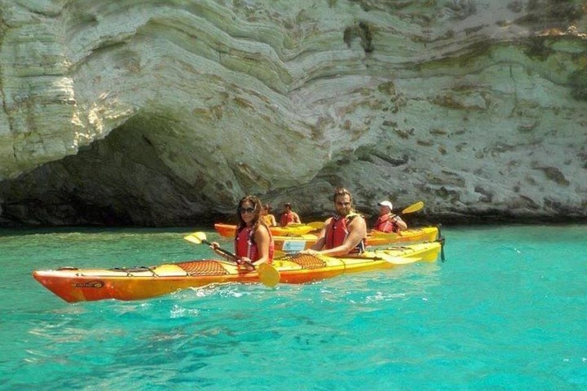 Eine Gruppe von Menschen paddelt mit dem Kajak in klarem türkisblauem Wasser, im Hintergrund eine weiße Felsformation. 4