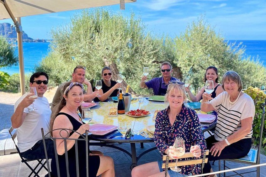 A group of people seated at an outdoor table with a view of the sea and trees. 2