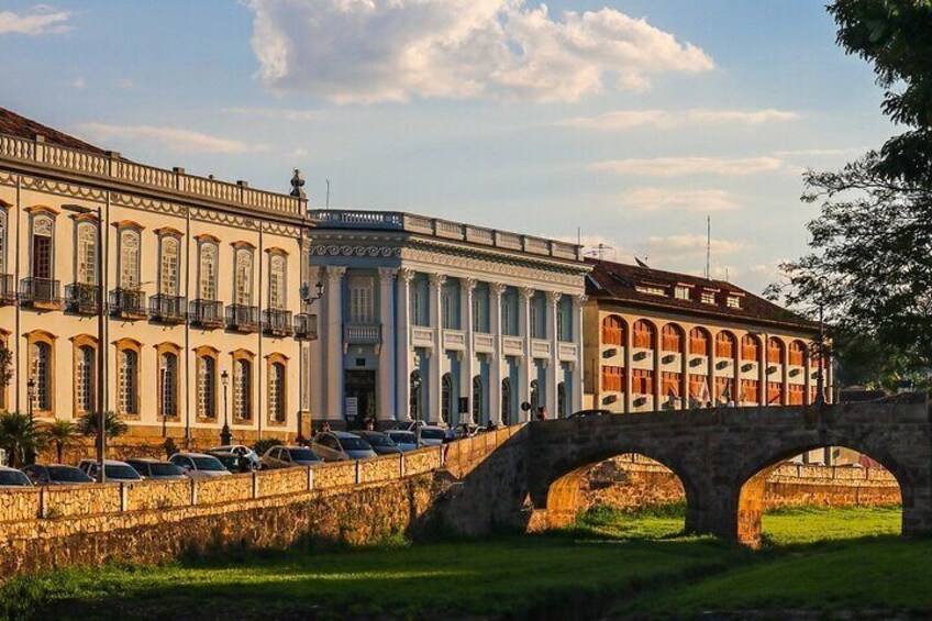 A stone bridge with arches, a row of parked cars, and classical buildings with columns and arched windows. 4
