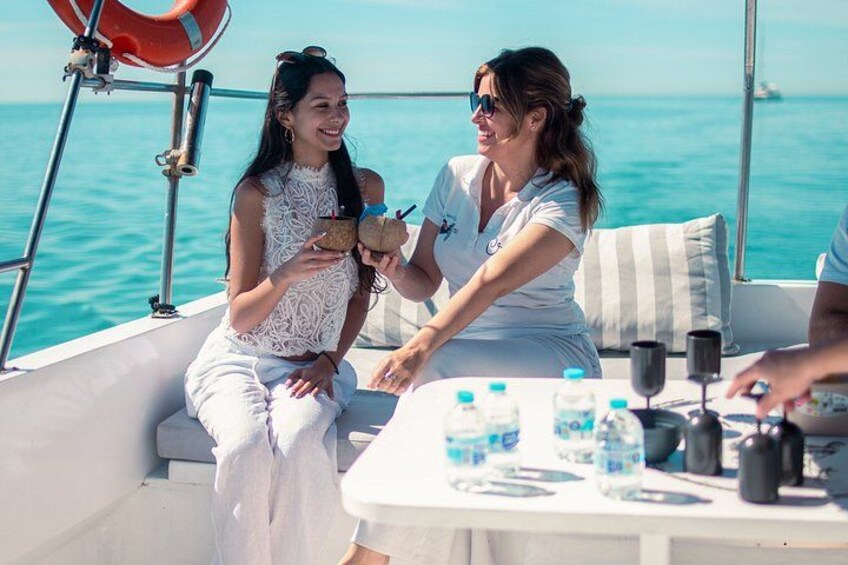 Two people on a boat, one holding a drink, with a table with bottles and a life preserver visible. 1