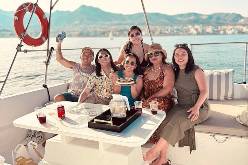 A group of people on a boat with a table, drinks, and a life preserver. 2