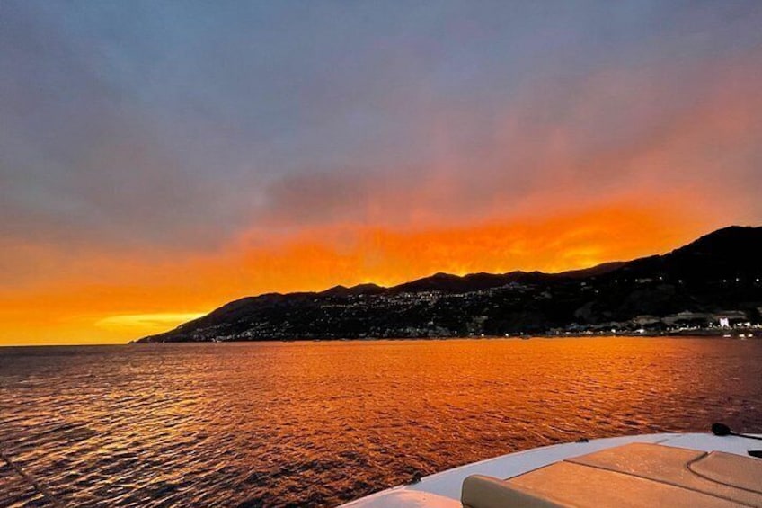A sunset over a body of water with a boat in the foreground and a mountainous coastline in the background. 1