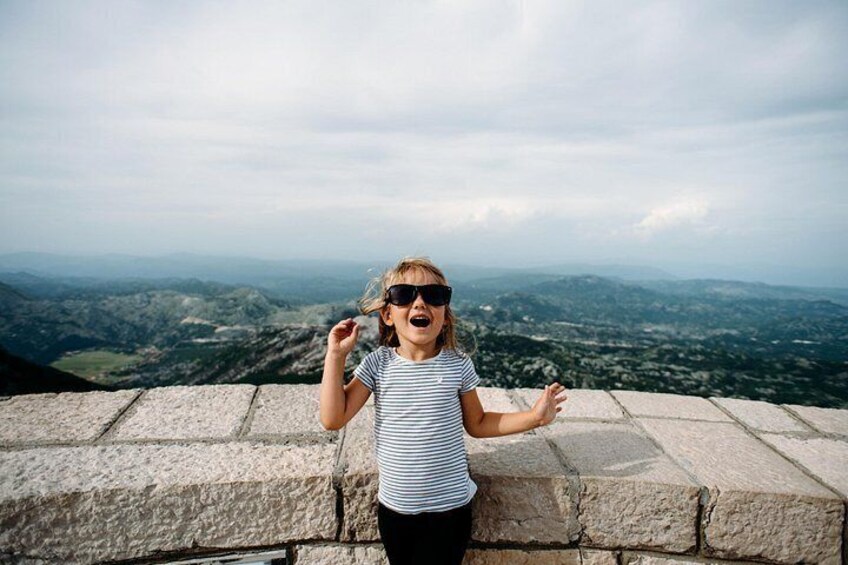 A person standing on a stone ledge with a panoramic view of a mountainous landscape. 2