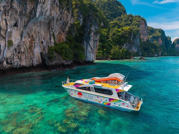 A boat named TIP-Top DESTINATION on clear turquoise water surrounded by rocky cliffs. 1