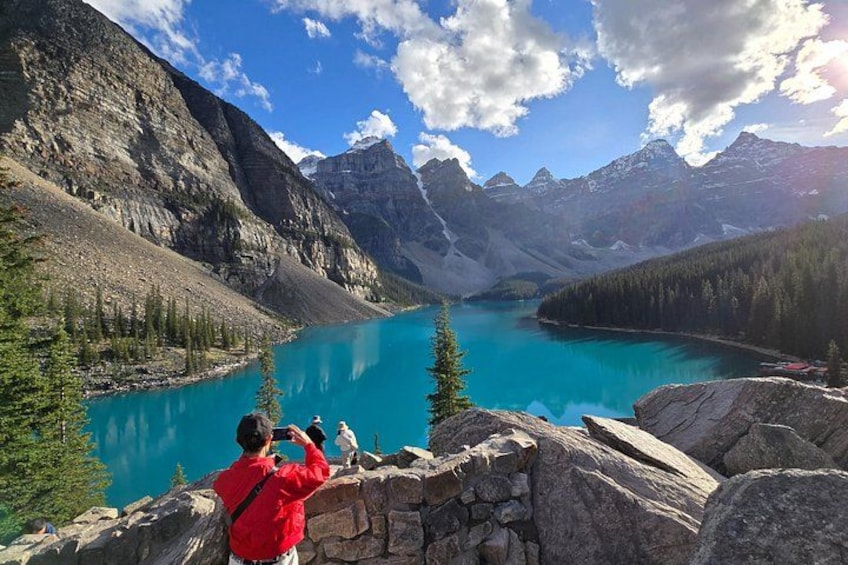 A person taking a photo of a turquoise lake surrounded by mountains. 4