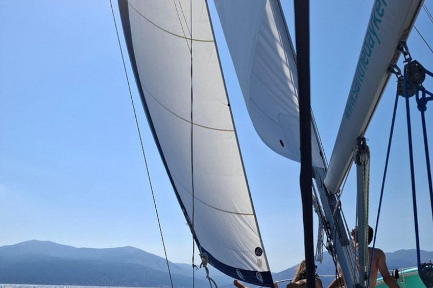 Una barca a vela con vele bianche, una persona al timone e un paesaggio montuoso sullo sfondo. 3
