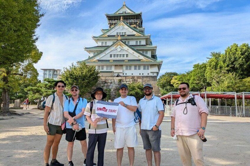 A group of people standing in front of a castle-like building with a sign that reads 'SINGHAI TOURS'. 1