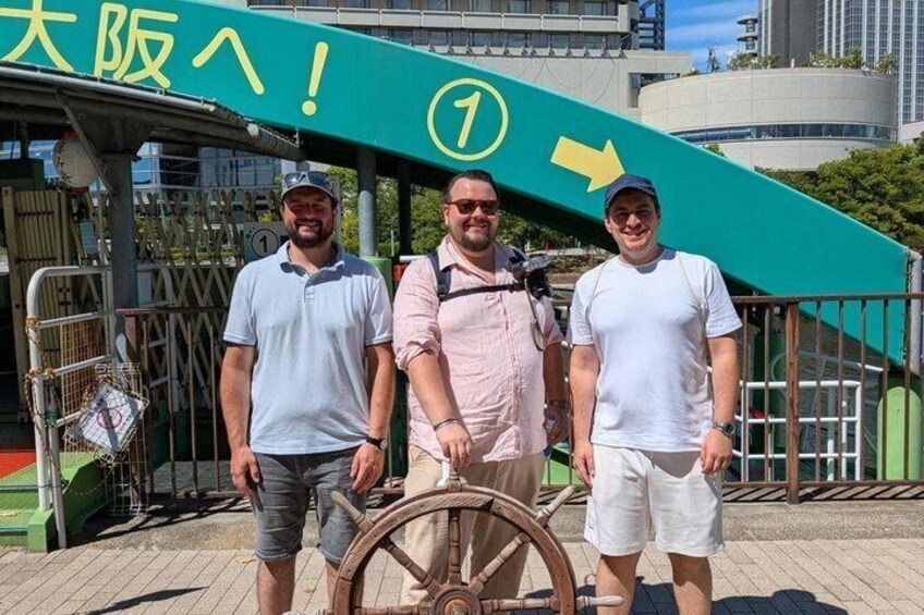 Three people standing in front of a green sign with a yellow arrow and the number 1. 5