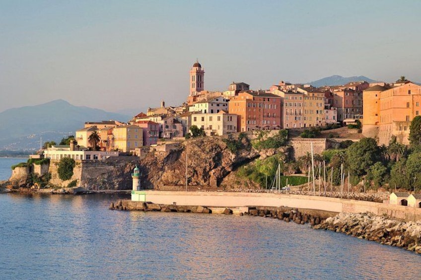 A coastal town with buildings, a lighthouse, and a rocky shoreline. 1