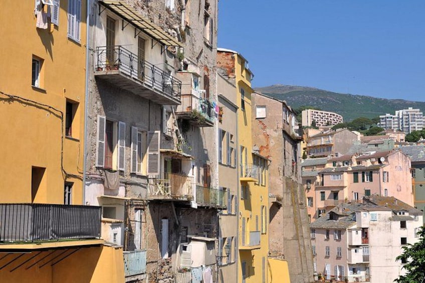 A row of colorful buildings with balconies, a clear sky, and a mountain in the background. 2