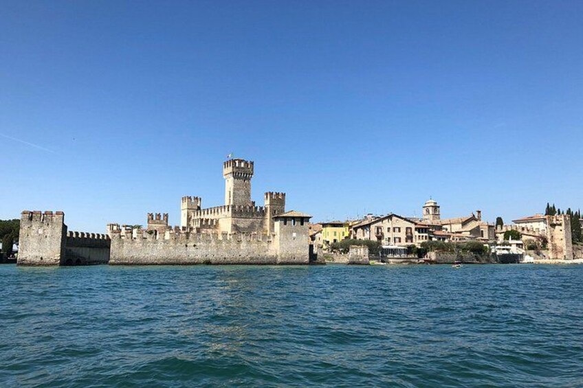Un castello storico con una torre imponente, circondato da un muro fortificato e edifici adiacenti. 2