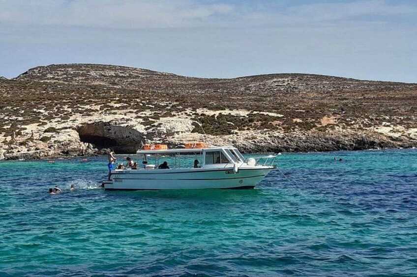 A boat on turquoise water with a rocky coastline and a hill in the background. 2