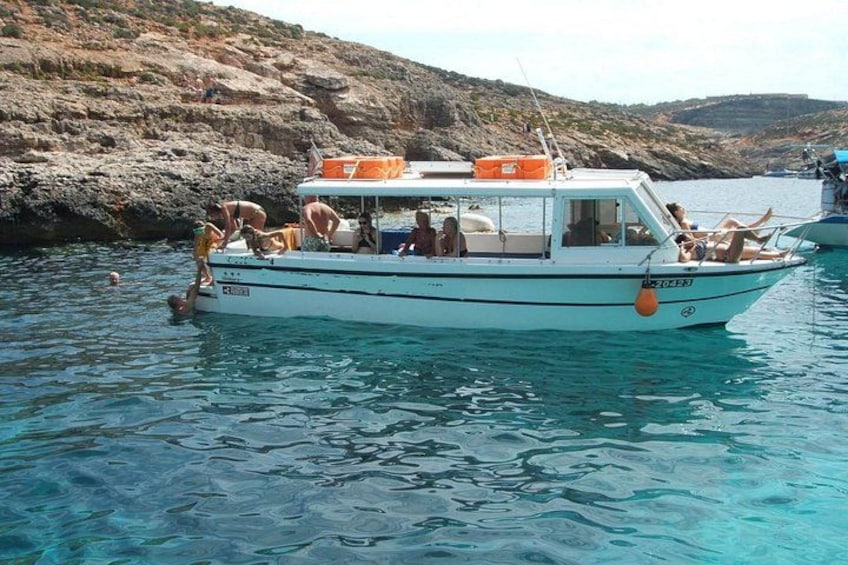 A boat with people on it, water, and rocky landscape in the background. 1