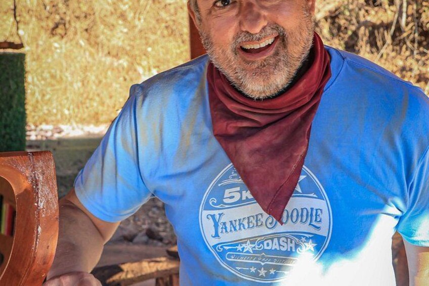 A person wearing a blue t-shirt with a graphic and text, sitting outdoors with a wooden chair visible. 2