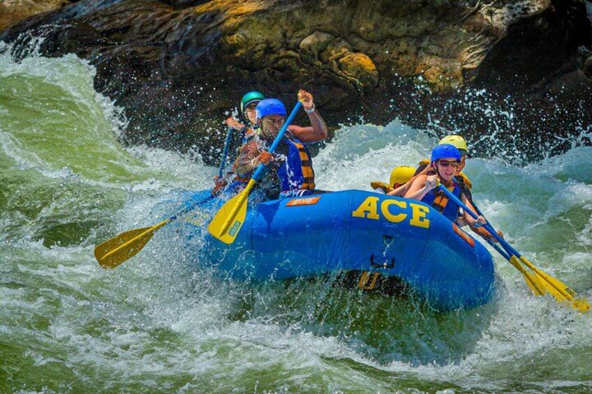 Two people in a blue raft labeled 'ACE' navigating through whitewater rapids. 1