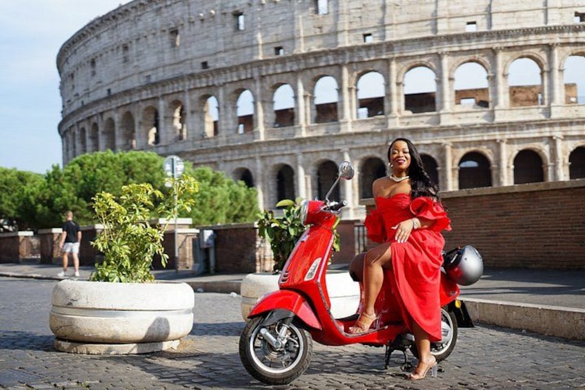 A person in a red dress sitting on a red scooter in front of the Colosseum. 5