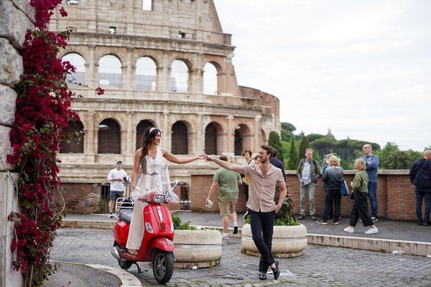 A couple on a red scooter in front of the Colosseum, with tourists in the background. 5