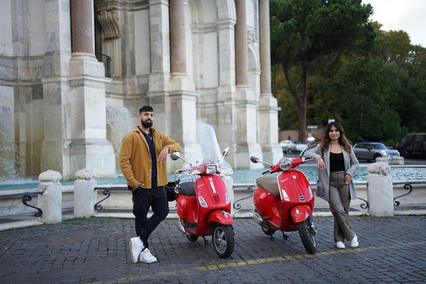 Two people standing next to a red scooter in front of a classical building with columns. 4
