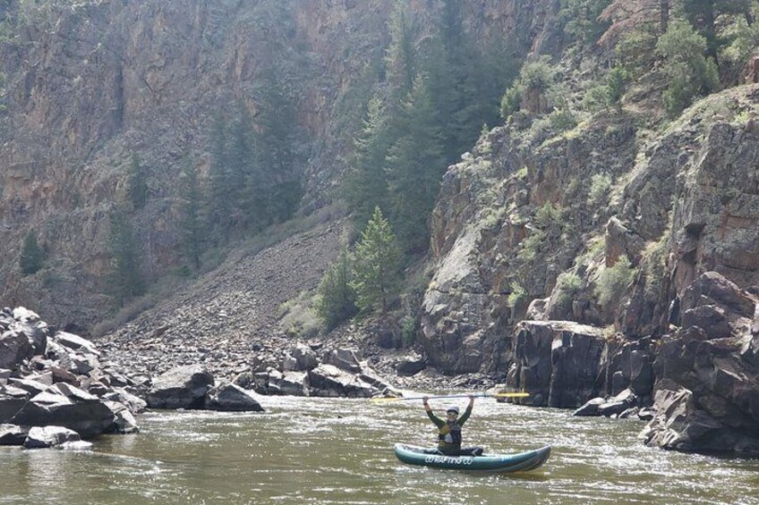 A river with a person kayaking, surrounded by rocky cliffs and sparse vegetation. 1