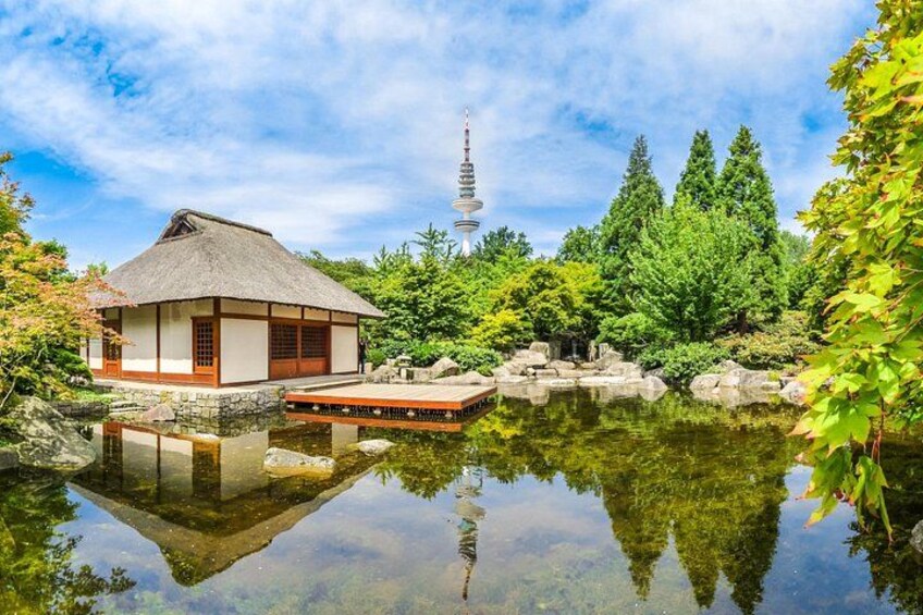 Un bâtiment traditionnel japonais, doté d’un toit de chaume, avec un étang qui reflète son architecture et une tour en arrière-plan. 3
