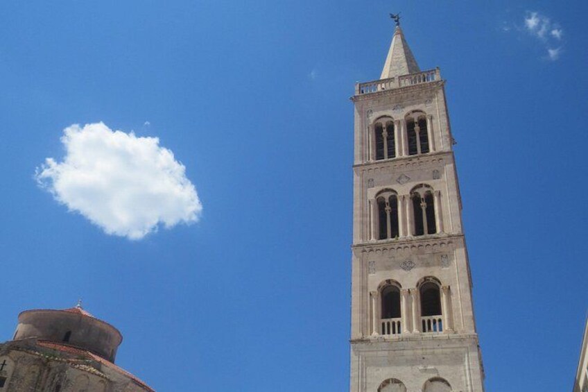 Une haute tour coiffée d’un toit en flèche et dotée de fenêtres en arc de cercle, se dressant sur un ciel bleu dégagé. 2
