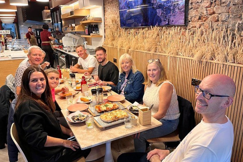 Un grupo de personas cenando en un restaurante, con pizza y bebidas sobre la mesa. 3