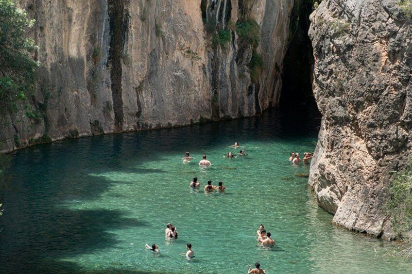 A group of people swimming in a clear, turquoise body of water surrounded by rocky cliffs. 3