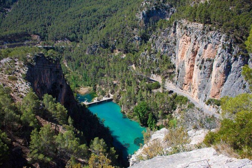 A turquoise lake surrounded by forested cliffs and a winding road. 2