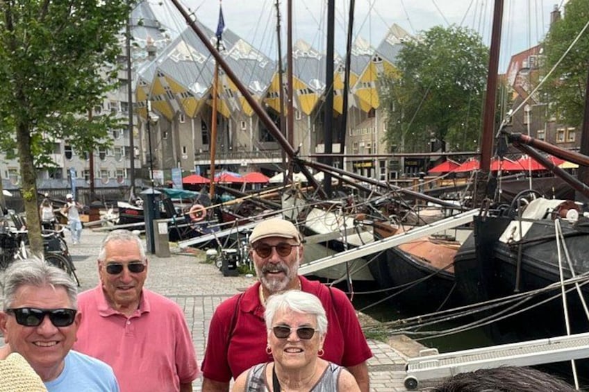 A group of people standing by a dock with boats and a building with yellow flags in the background. 2