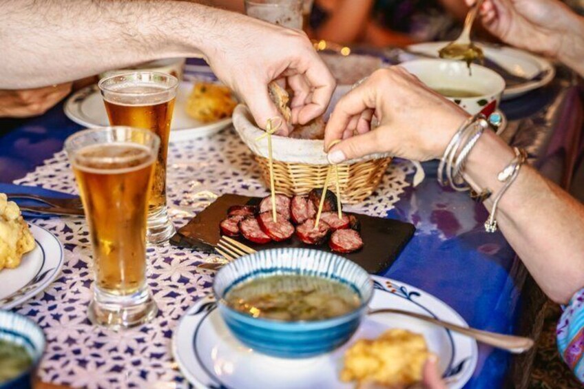 A person holding a skewer with food, a glass of beer, and a bowl of soup on a table. 2