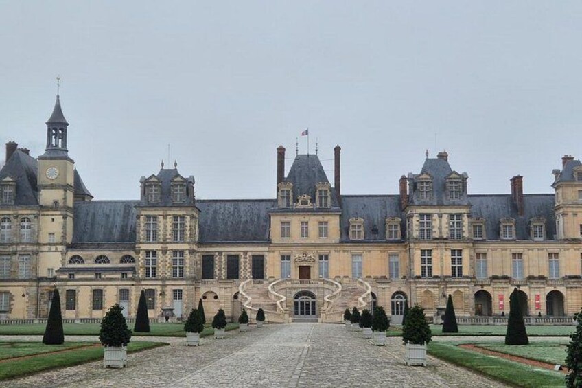 A large historic building with a symmetrical facade, a central staircase, and a formal garden with trimmed hedges. 5