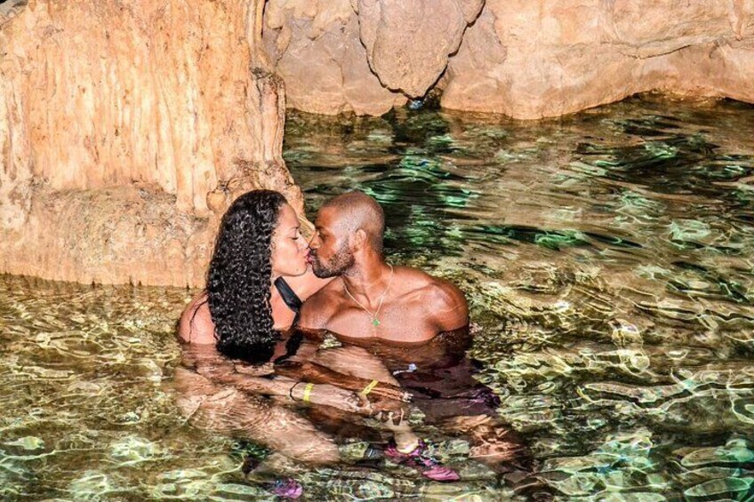 A couple in a natural pool with clear water, surrounded by rocky terrain. 1