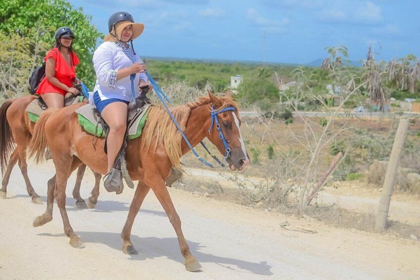 Dos personas cabalgando por un sendero de tierra con vegetación escasa y cielo despejado. 2