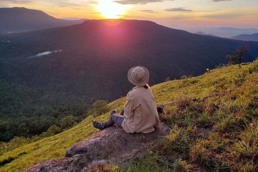A person sitting on a rock with a view of a valley and mountains during sunset. 5