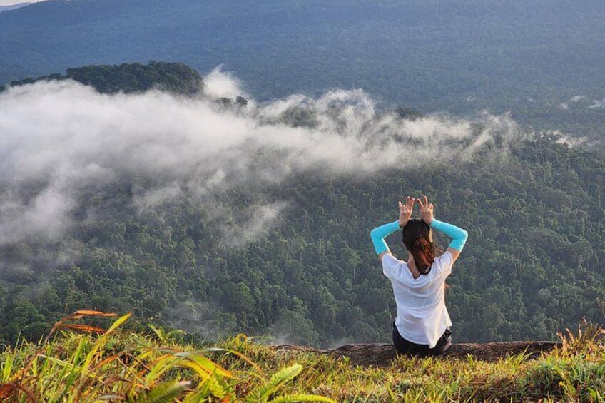 A person meditating on a grassy hill overlooking a forested valley with mist. 4