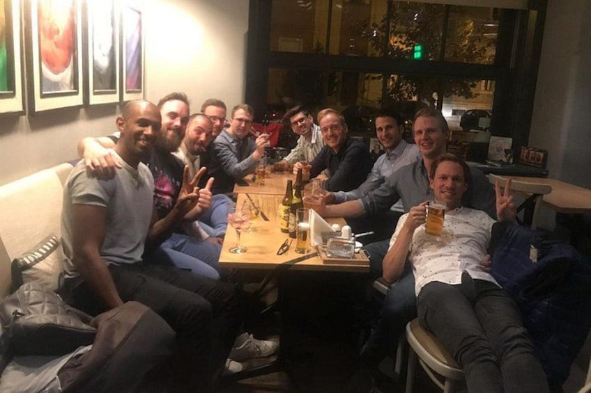 A group of people sitting around a table with drinks, in a dimly lit indoor setting. 3