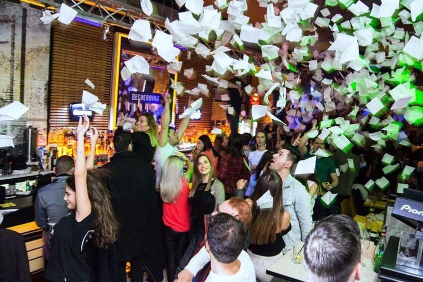 A crowded indoor event with people celebrating, some holding up papers. 5